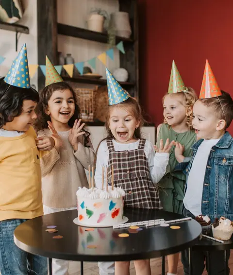 Children in party hats round a birthday cake